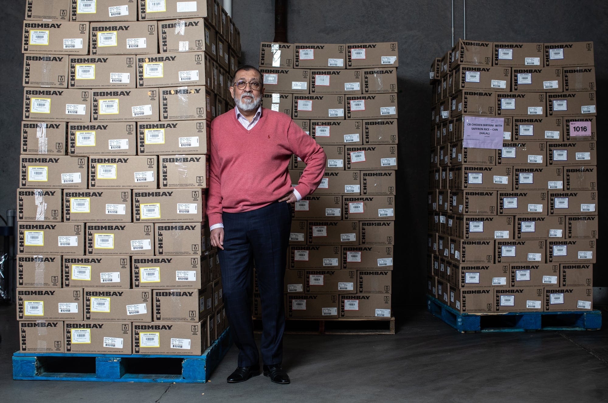A man in a pink sweater and black slacks standing in a storeroom filled with boxes