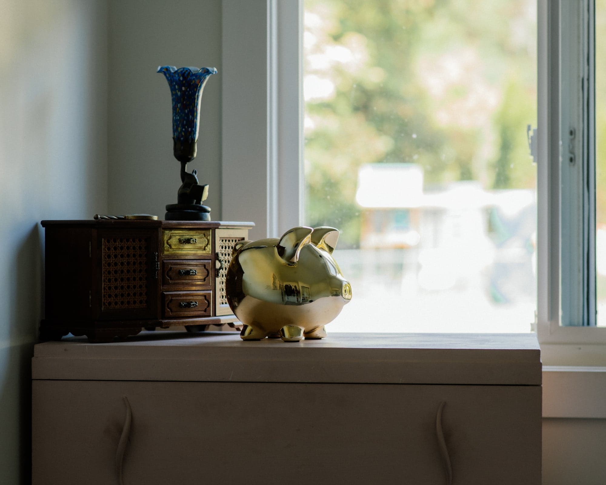 A piggy bank on a dresser beside a window