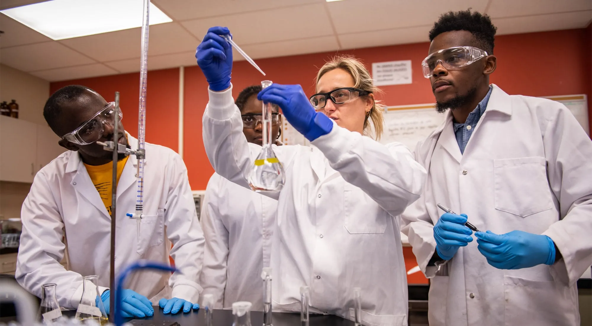 Four students in lab coats and gloves conducting an experiment.