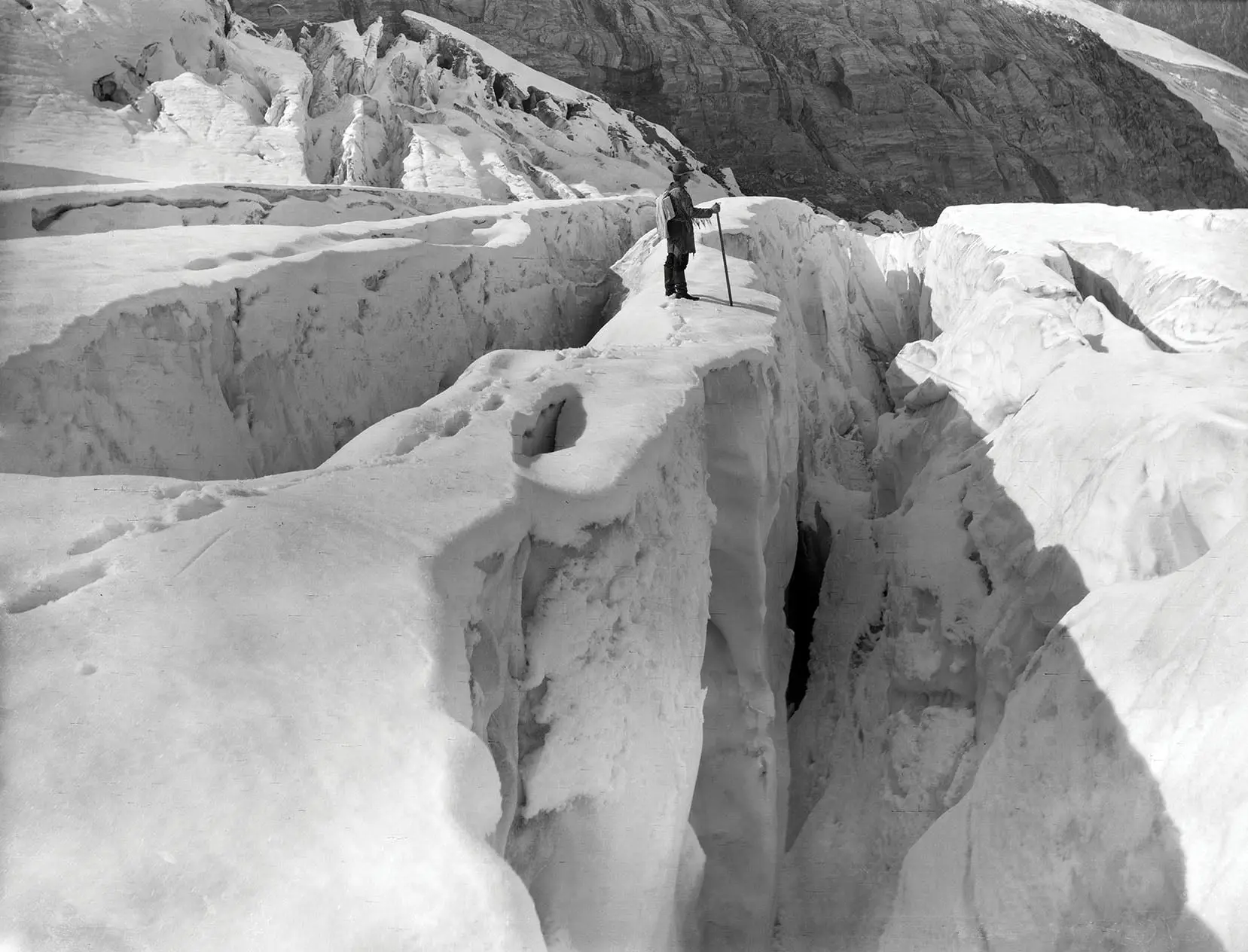 A person in a hat standing at the edge of a ravine, holding a walking stick