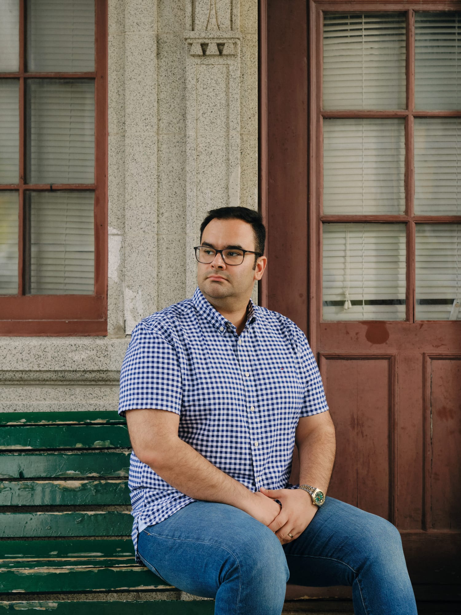 A man in a blue shirt sitting in front of a house