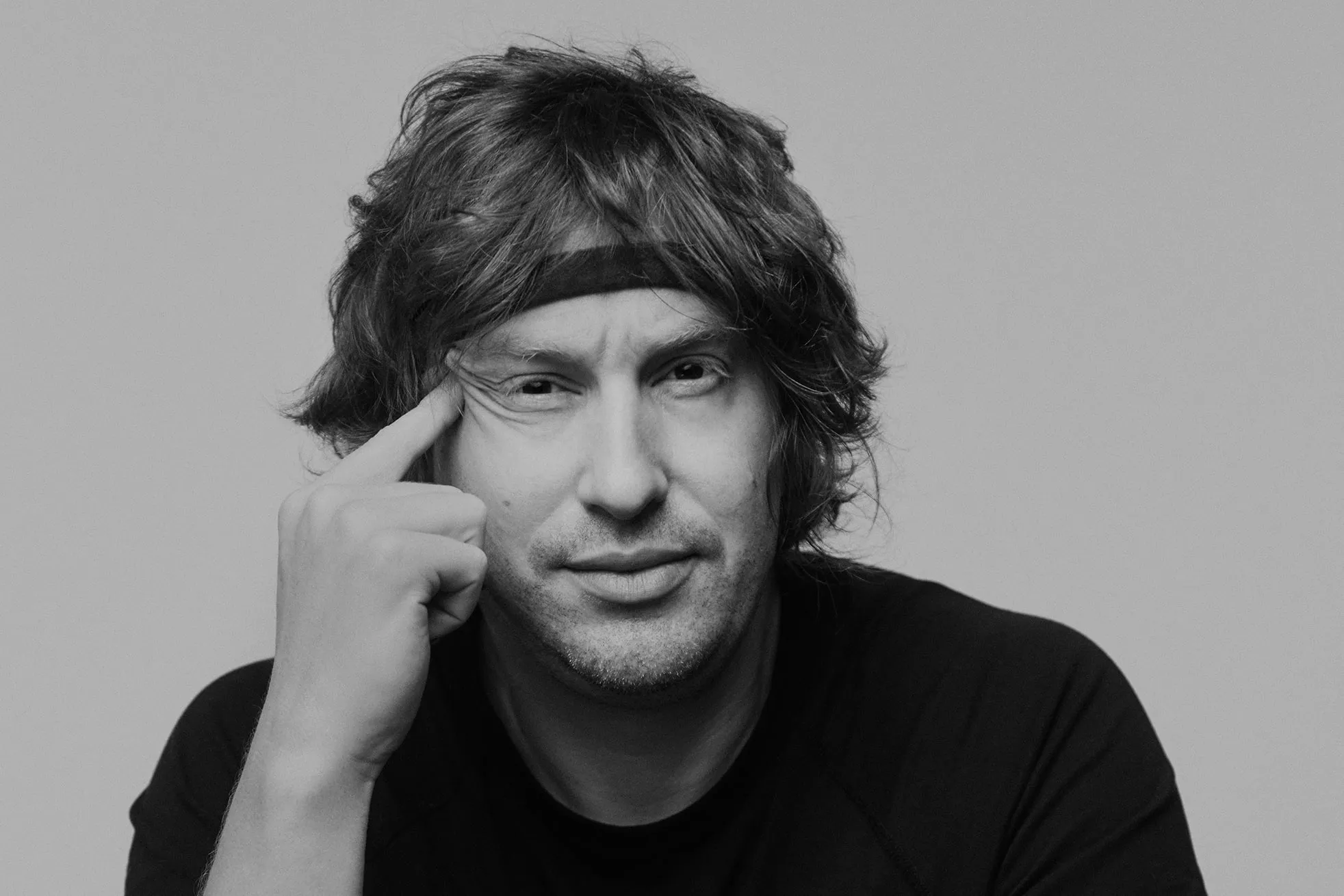 A man with curly hair wearing a black sweatband and a black t-shirt
