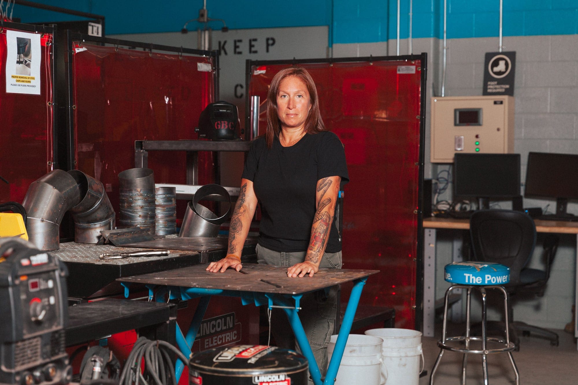 A portrait of Lilly standing in a welding lab, behind a workstation.
