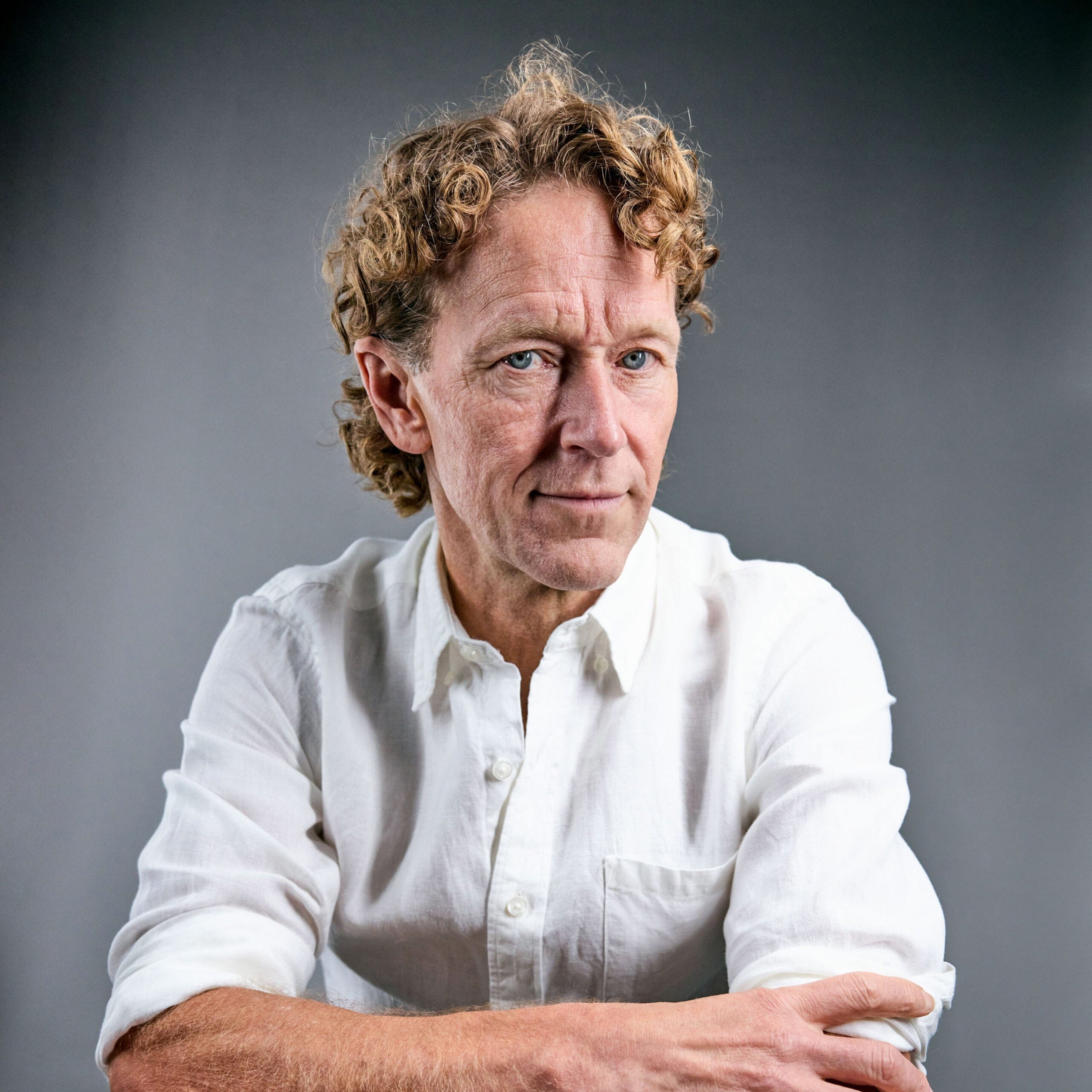 A curly-haired man in a white shirt, with his arms crossed over his chest