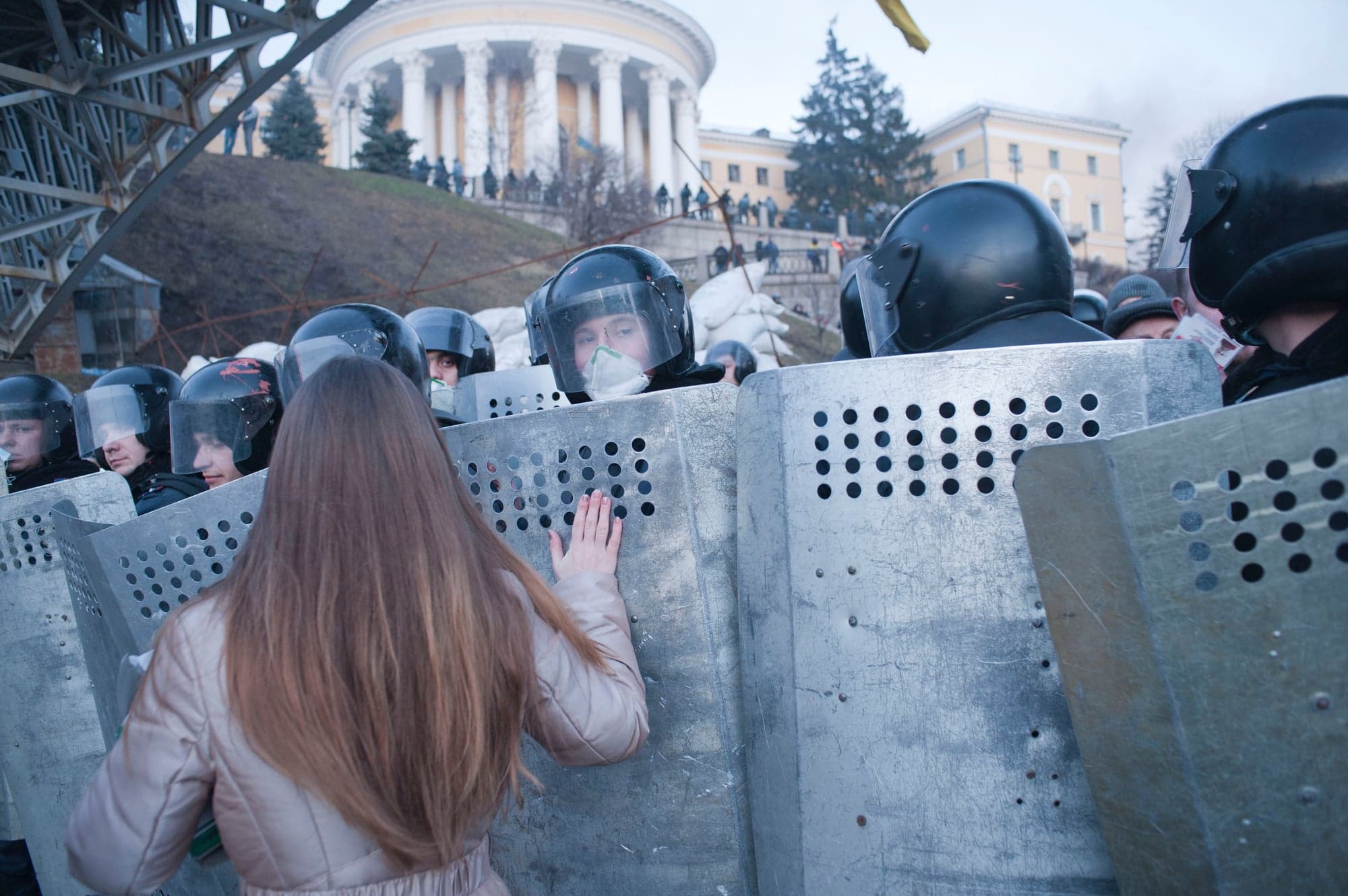 A demonstrator prays with her hand on a policeman's shield in front of a barricade in Independence Square