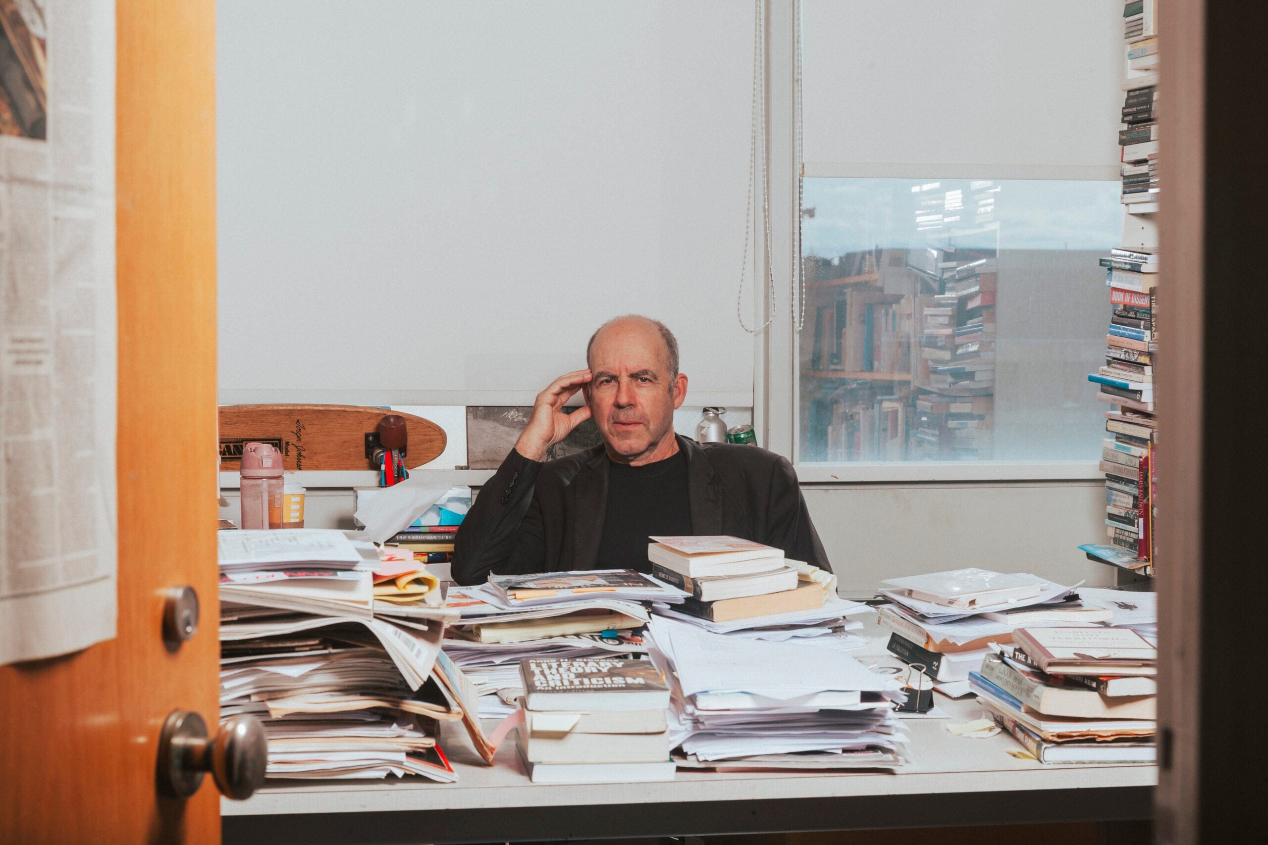 A university professor sitting at a desk piled high with books