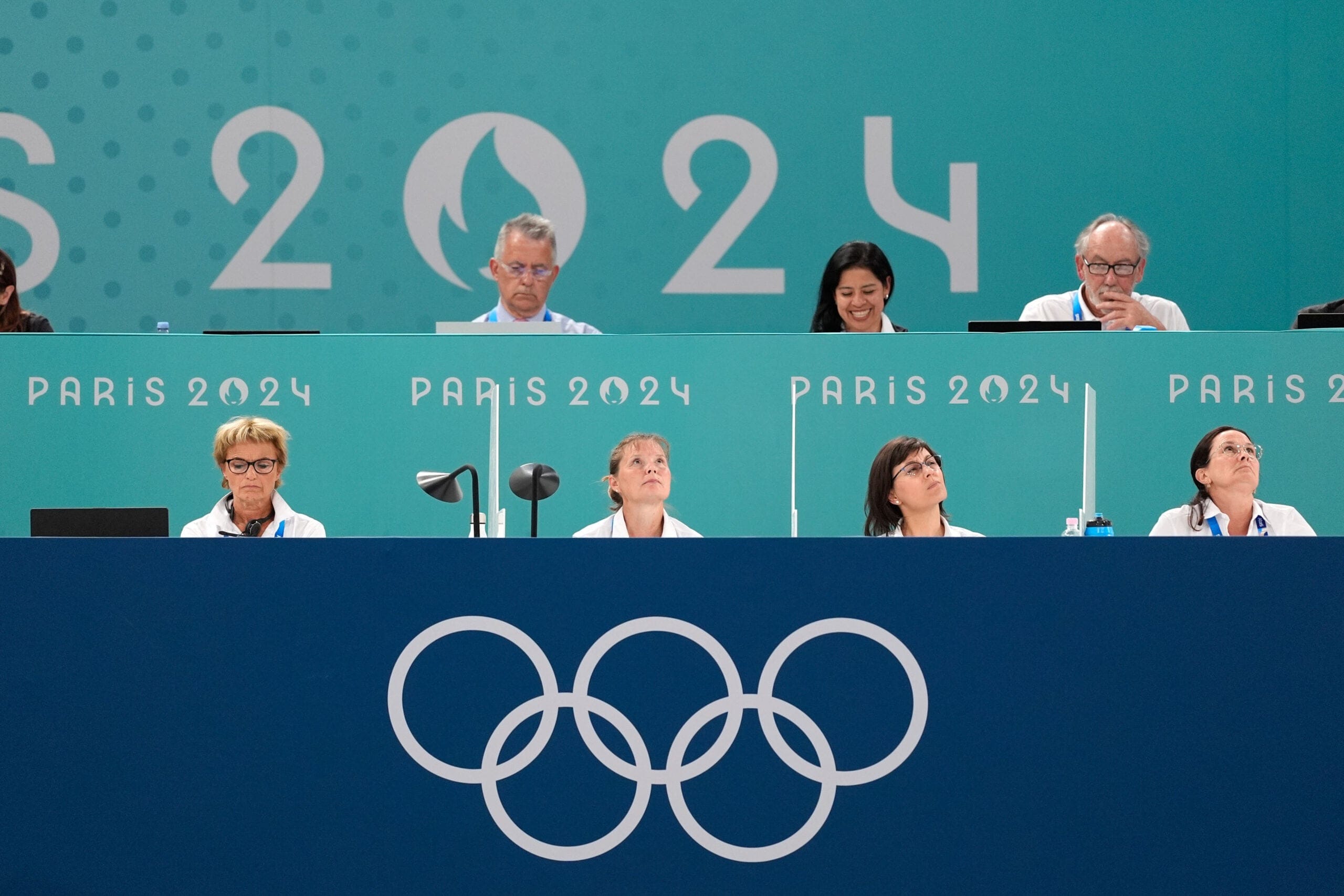 A panel of judges sitting behind a table that has the Olympic logo on it