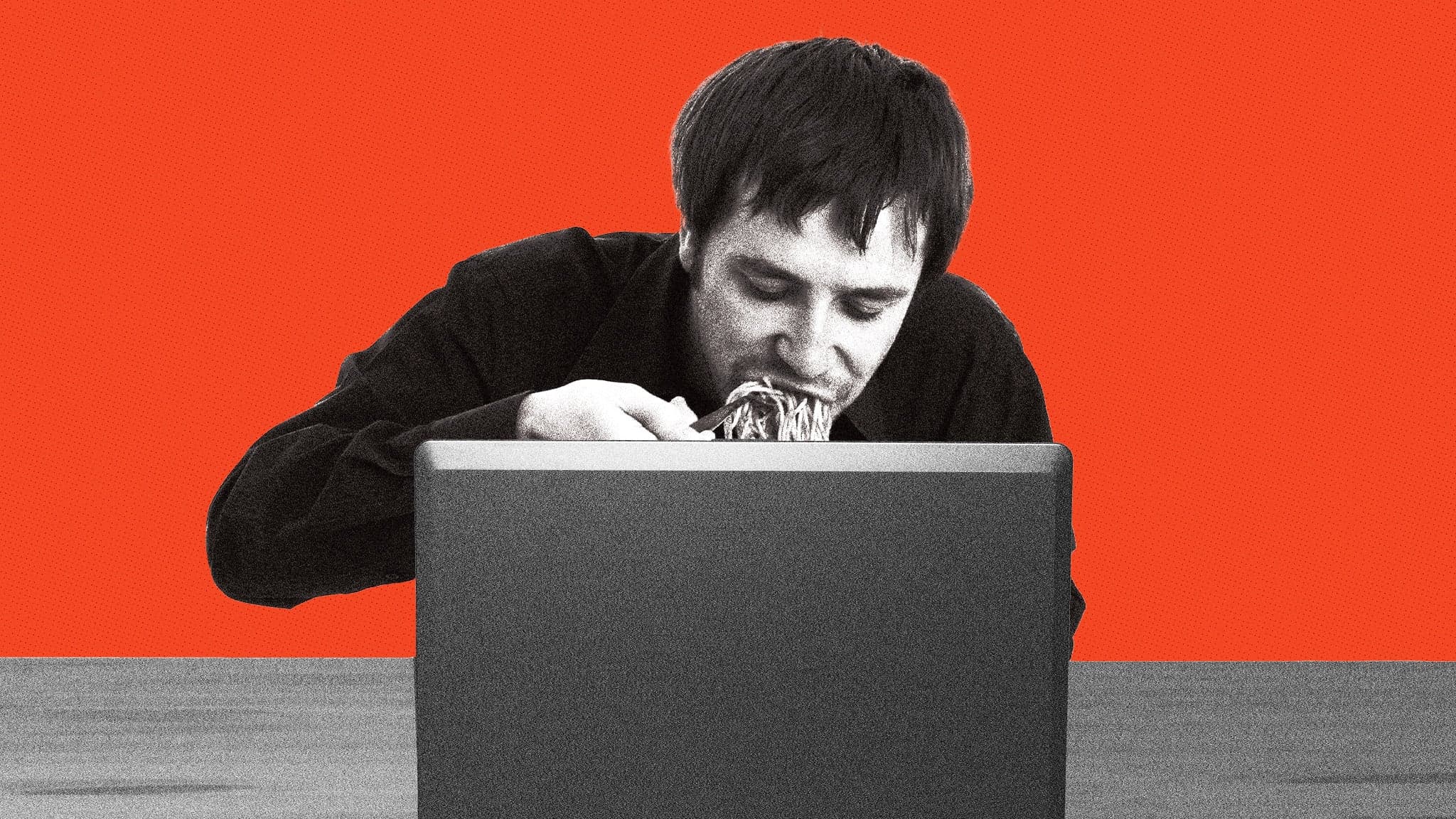 A person shoveling spaghetti into his mouth while sitting in front of a computer