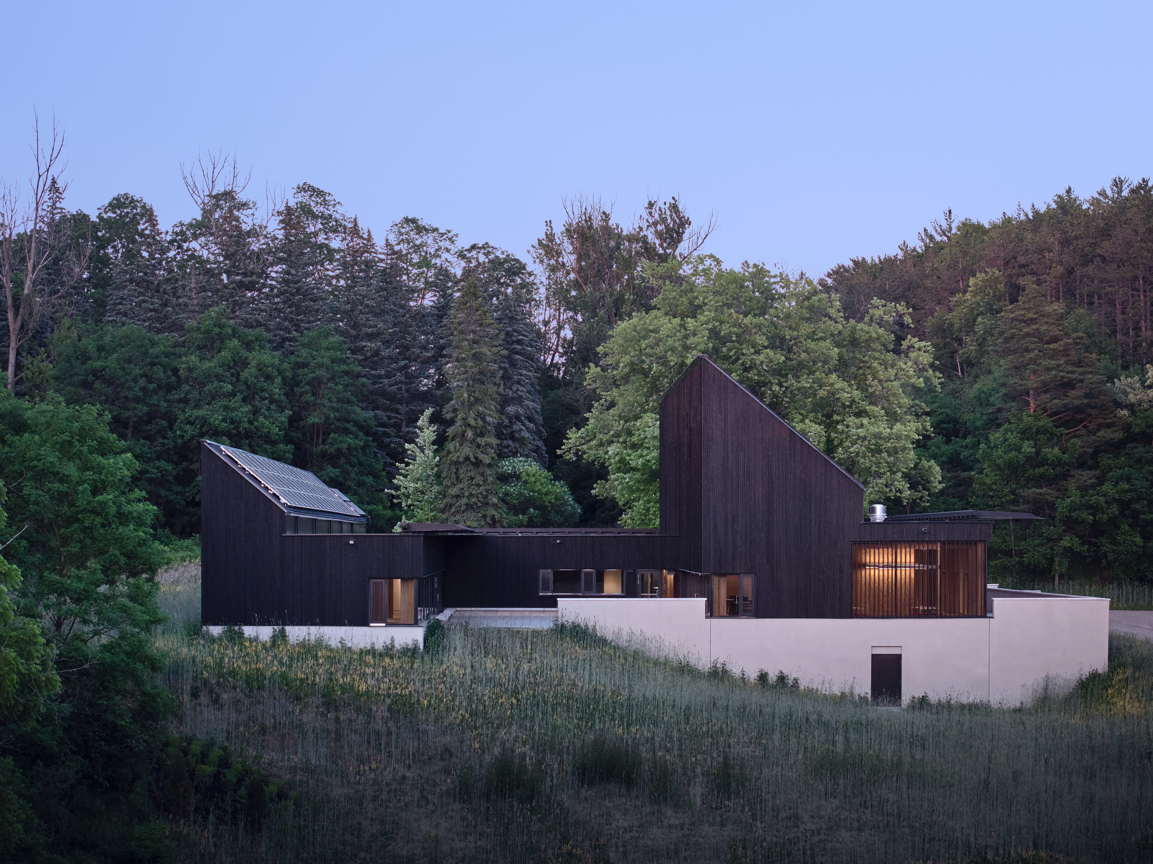 A modern and geometric black building with multiple wings and small illuminated windows among a forest
