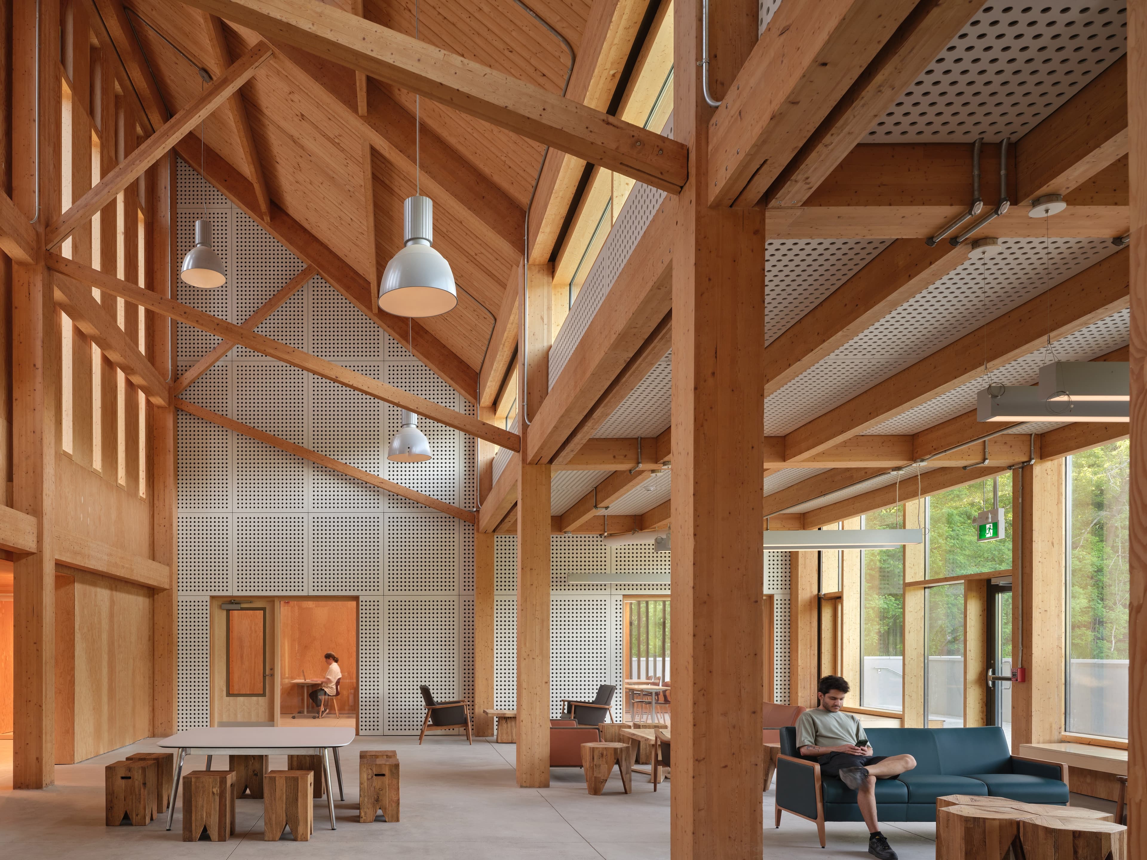 A large room with wood columns and a coffered wood ceiling and concrete floors. There is various seating around the space