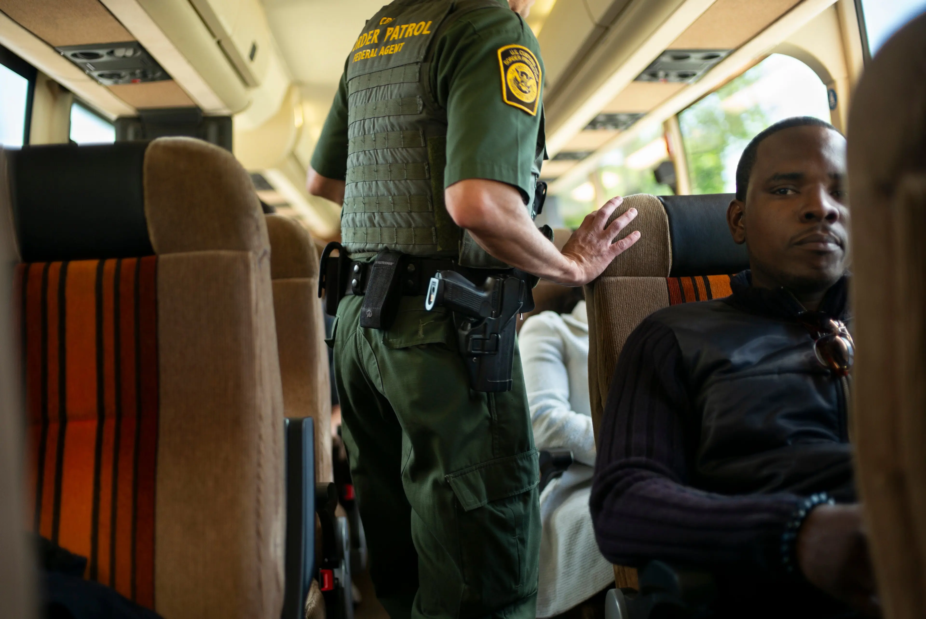 A uniformed officer walks up the aisle of a Greyhound bus