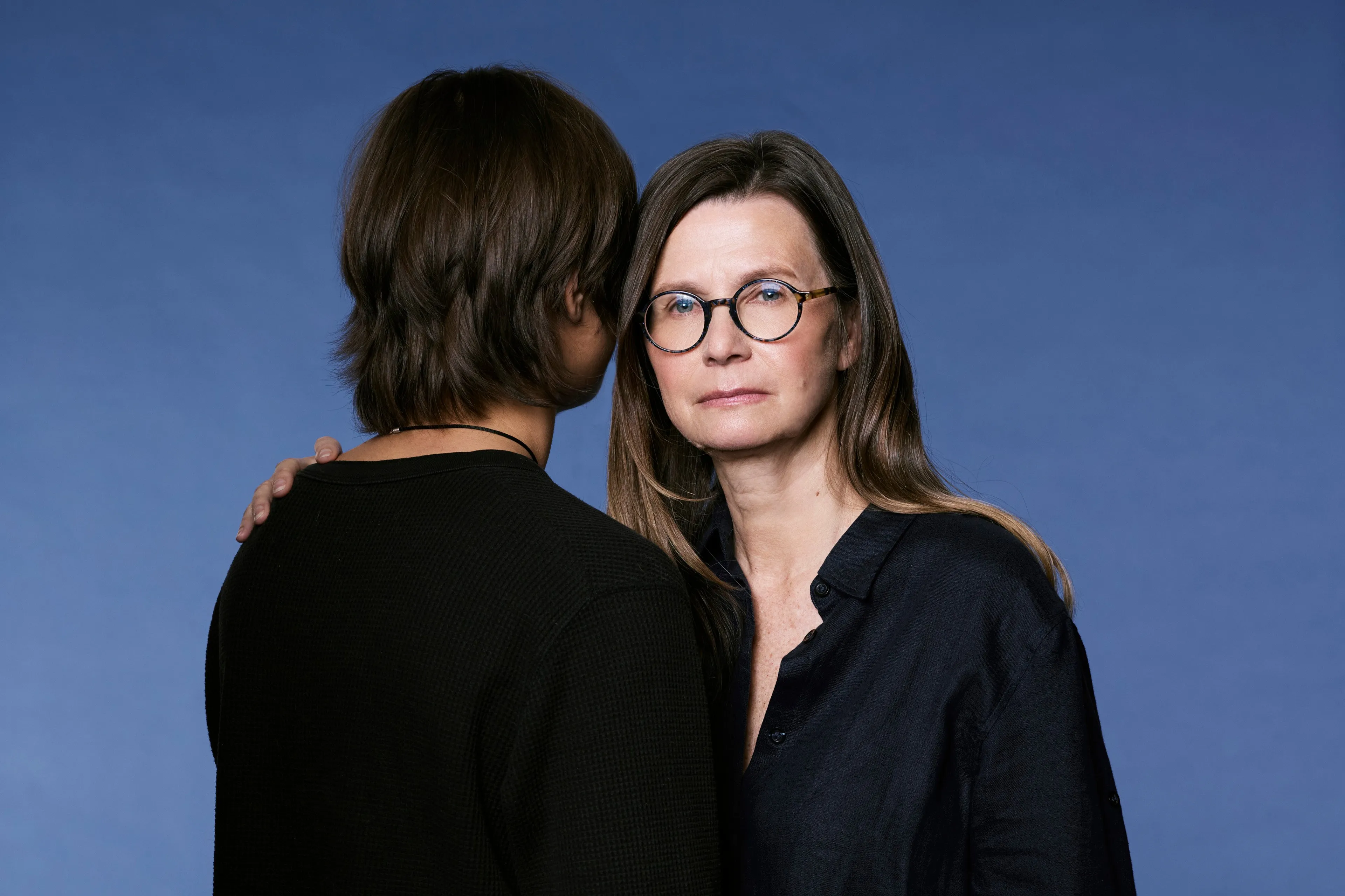A mother facing the camera, with an arm around her son who's facing away from the camera