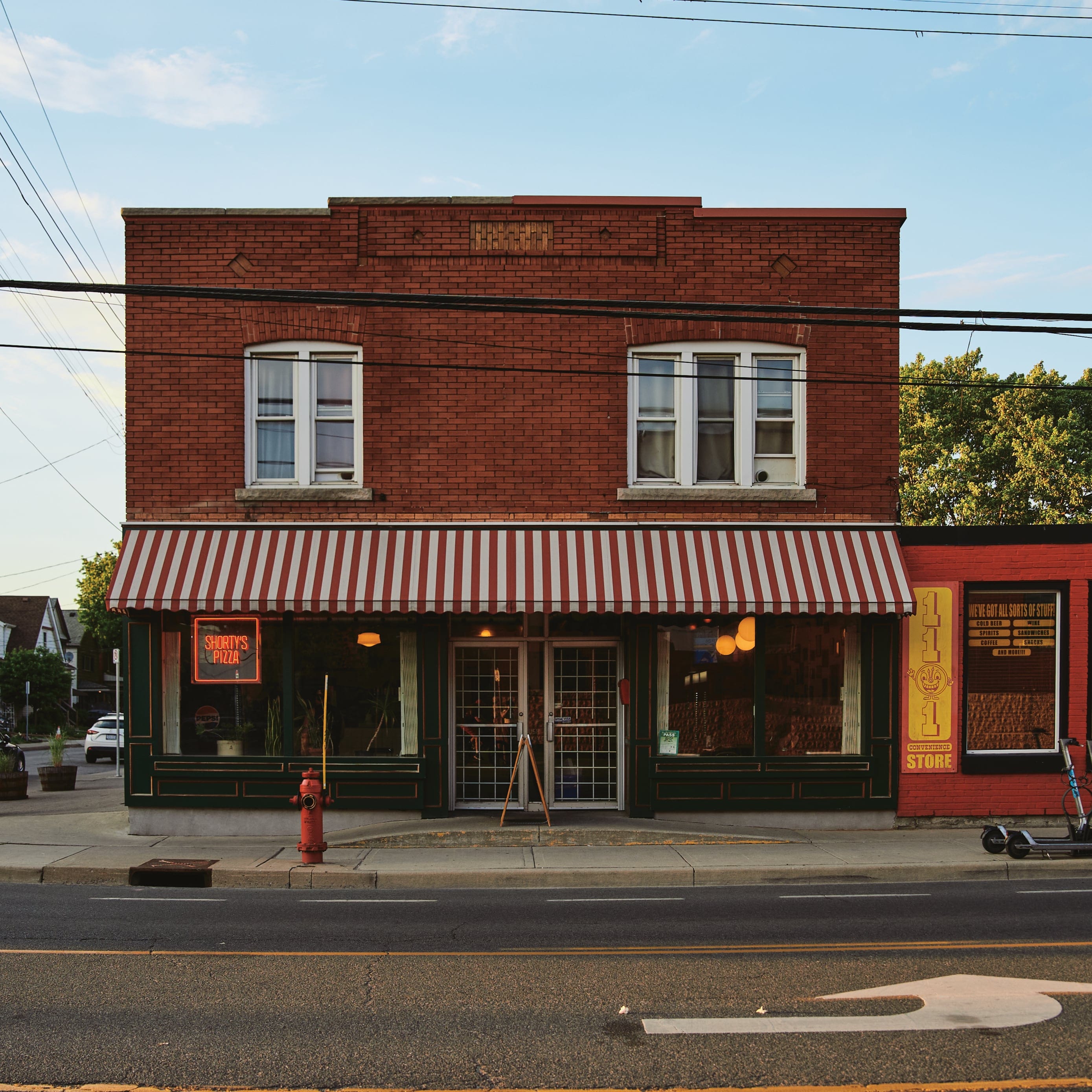 A front of a shop made of brick with a neon sign saying "Shorty’s Pizza"