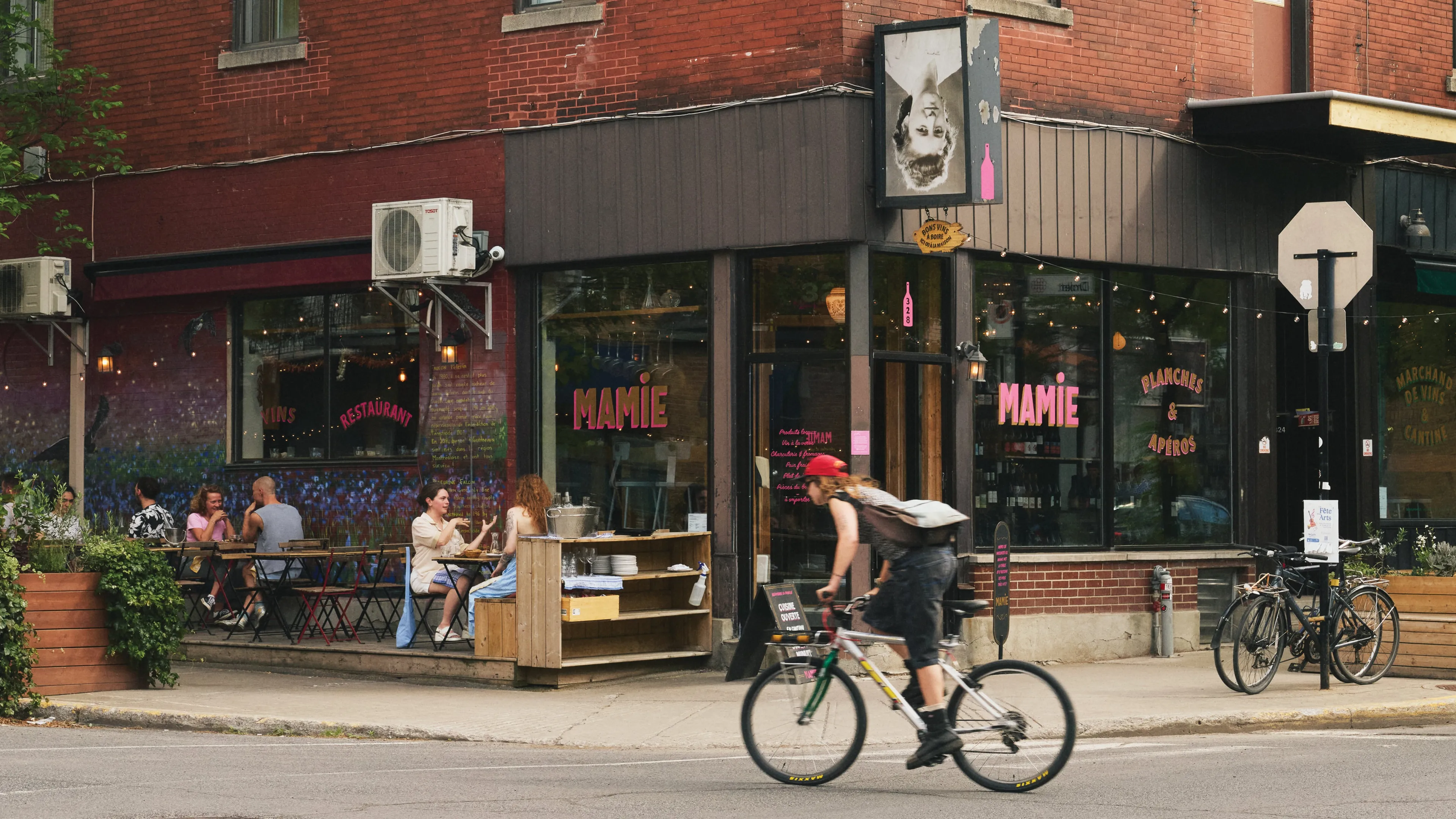 A person on a bicycle passing by the front of a brick building that says "Mamie" on its windows