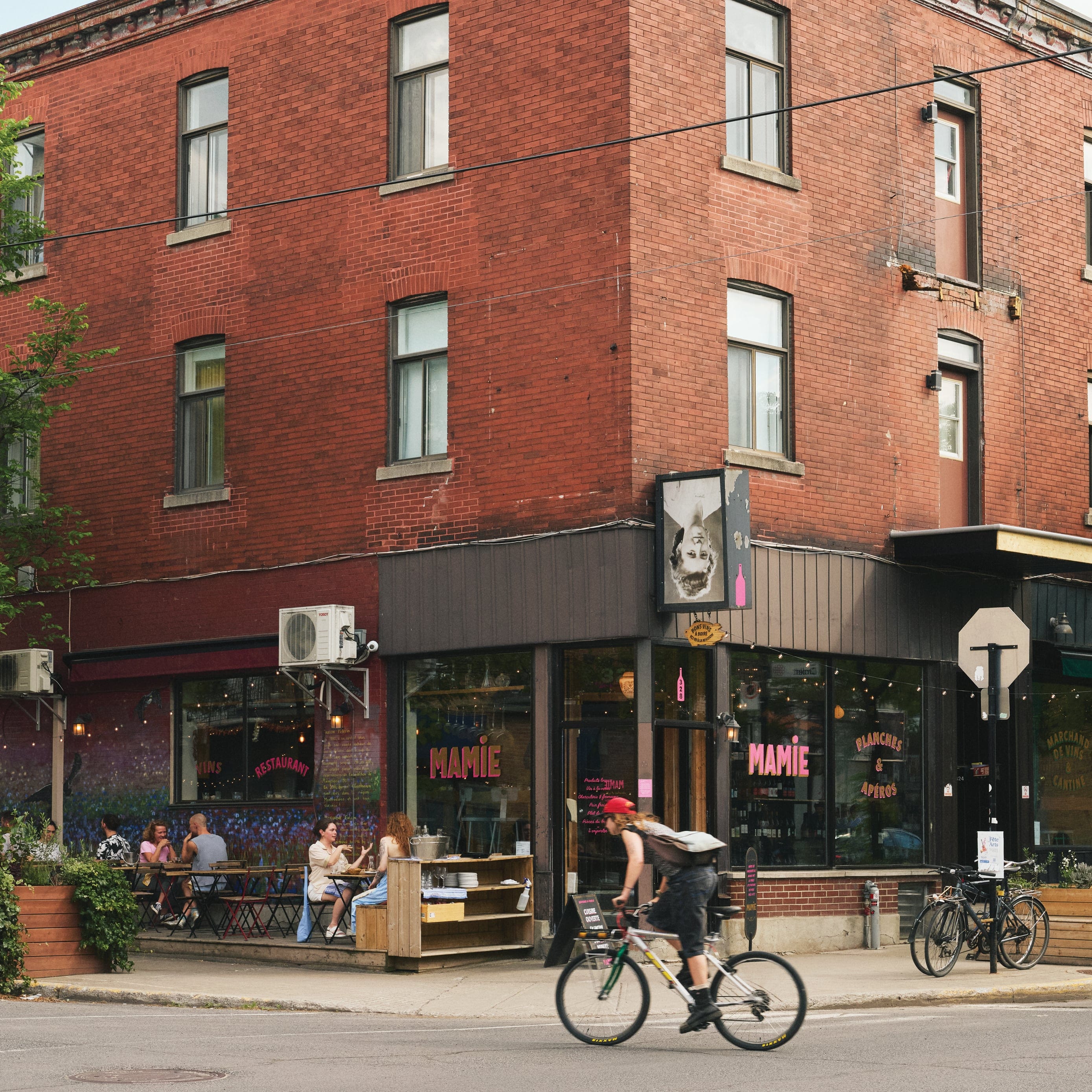A person on a bicycle passing by the front of a brick building that says "Mamie" on its windows