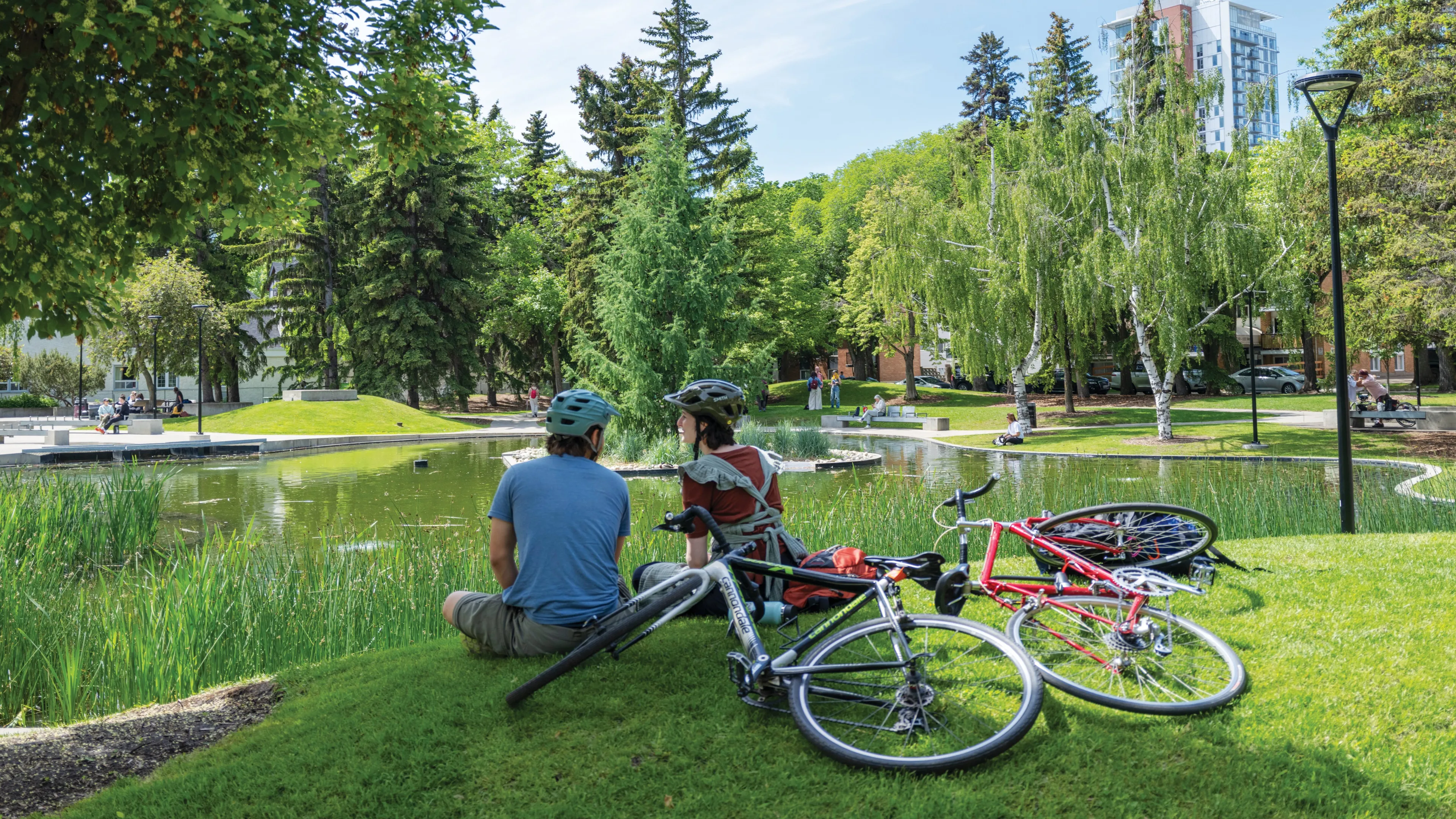Two cyclists sitting by the pond at a park