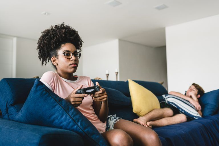 a girl wearing glasses playing video games on a couch (Igor Alecsander/Getty Images)