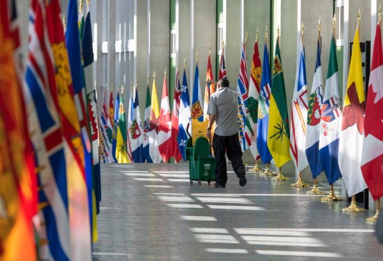 A custodian wheels a mop down the flag lined hallway at the John G. Diefenbaker Building, where Trudeau was set to attend the First Ministers' Meeting on March 12, 2020 (CP/Justin Tang)