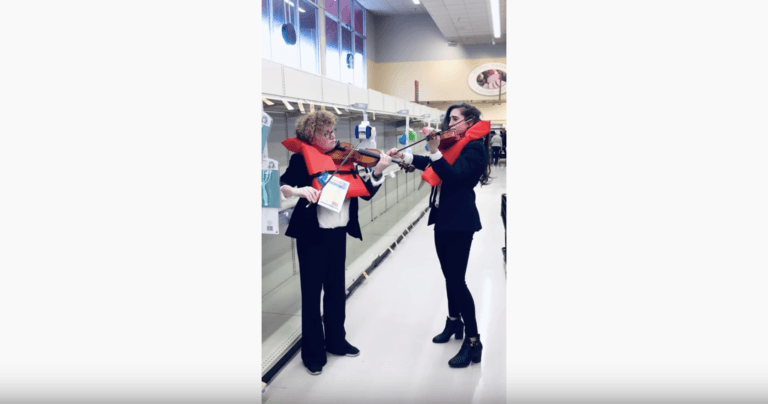 Two women don tuxedos and lifejackets and play the violin in an empty toilet paper aisle (Bonnie von Duyke/YouTube)