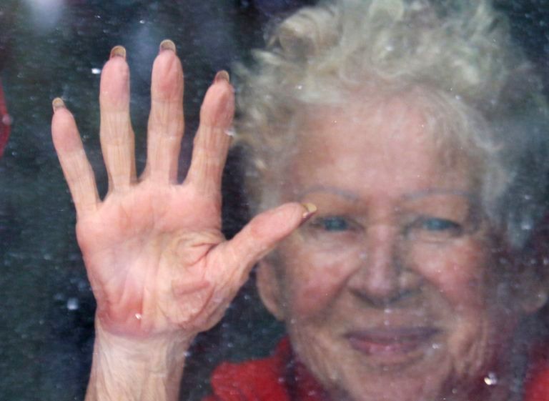 Resident Adeline Thrush, age 84, touches her window to acknowlege family and local residents showing up outside each afternoon to show caring and support for residents in isolation at a long term care centre in Calgary, Alberta on Apr. 2, 2020. (Larry MacDougal/CP)