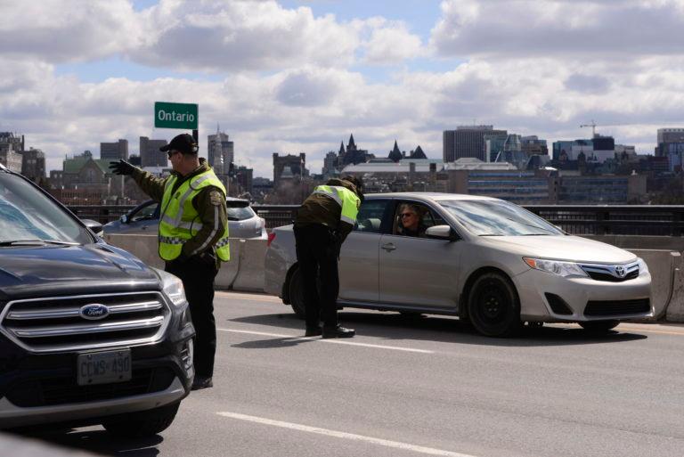 Quebec police officers randomly stop traffic entering Quebec from Ottawa on Wednesday; the province has also banned non-essential travel in some places within its borders. (Sean Kilpatrick/CP)