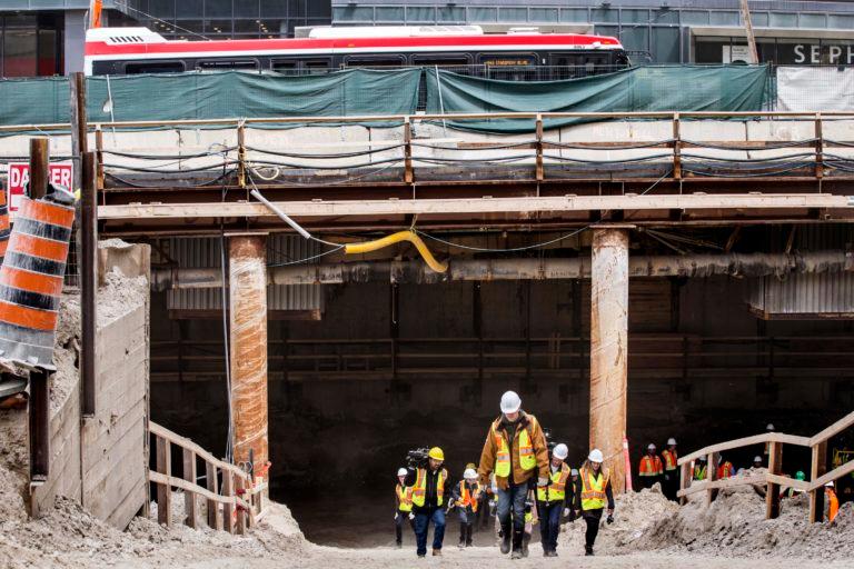 A TTC bus drives on Eglinton Ave. W. near Yonge St., as media climb a dirt construction ramp leading to the underpinning of the new Eglinton Crosstown Light Rail Transit (LRT) project. (Getty Images)