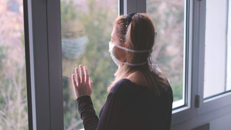 Woman wearing face mask looking out a window