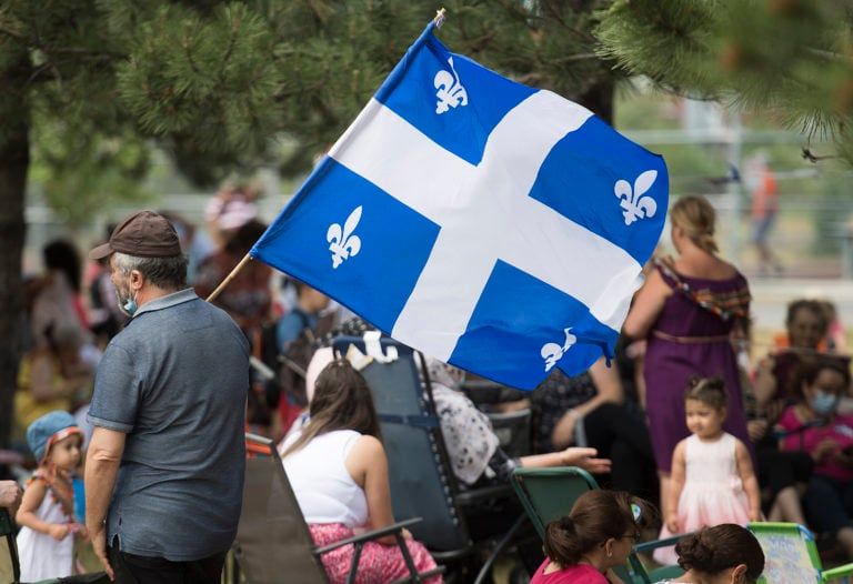 A man holds a Quebec flag as people gather in a city park on St-Jean Baptiste Day in Montreal on June 24, 2020. (Graham Hughes/CP)