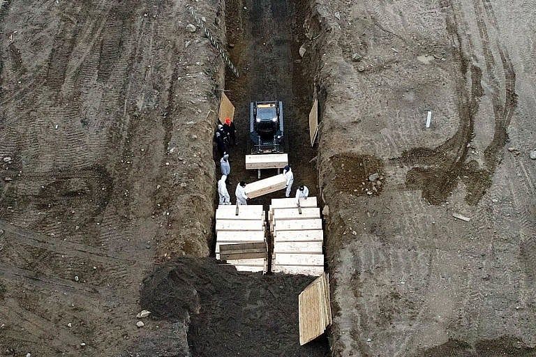 Workers in personal protective equipment bury bodies in a trench on Hart Island in New York during the state’s spring surge of coronavirus deaths (John Minchillo/AP/CP)