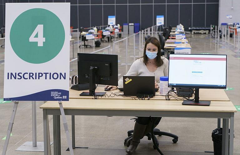 A health care worker works at setting up a registration booth at a vaccination clinic in Montreal, on Monday, February 1, 2021. THE CANADIAN PRESS/Paul Chiasson