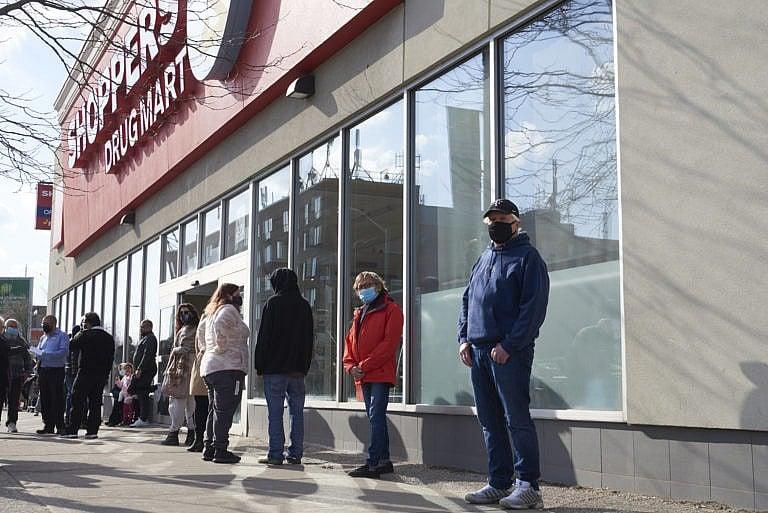 Customers wait to get into the Shoppers Drug Mart at Danforth and Coxwell as people in the age group of 60-64 line up on the other side of the store to await their Oxford-AstraZeneca COVID-19 vaccinations, in Toronto on March 11, 2021. THE CANADIAN PRESS IMAGES/Rachel Verbin