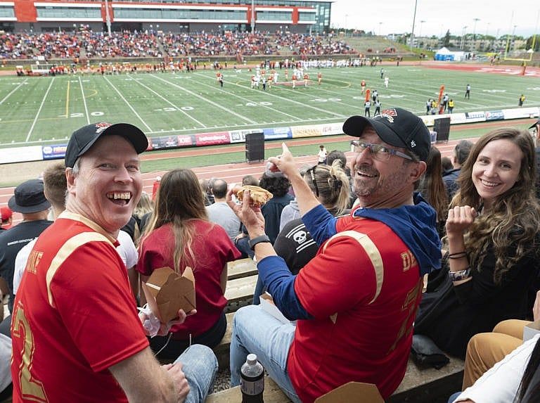 Bloc Quebecois Leader Yves-Francois Blanchet, centre, enjoys a hot dog while attending a Laval University Rouge et Or football game against McGill Red Birds with local candidates Marc Dean, left, and Marie-Christine Richard, Sunday, August 29, 2021 in Quebec City. Dean's son, Marc-Antoine Dean Rios plays the offensive line for the Rouge et Or at Laval University. (Jacques Boissinot/CP)