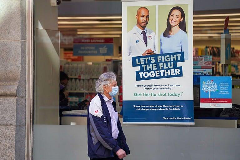 <p>A pedestrian walks by a sign in a store window encouraging people to receive a seasonal flu shot in Toronto on Tuesday, October 19, 2021. THE CANADIAN PRESS/Evan Buhler</p>
