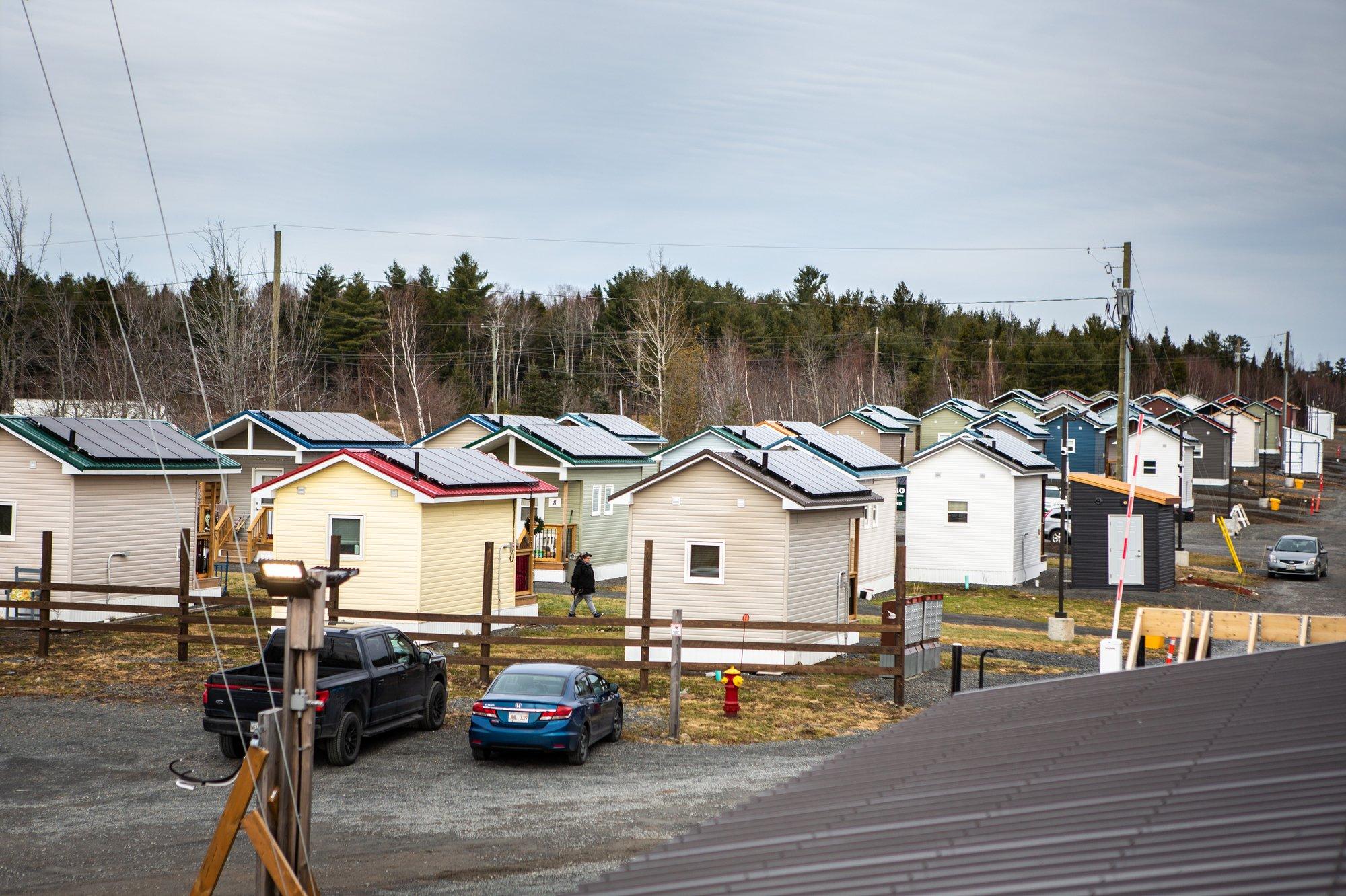 A photo of a cluster of tiny light-coloured homes against the backdrop of a forested hill behind