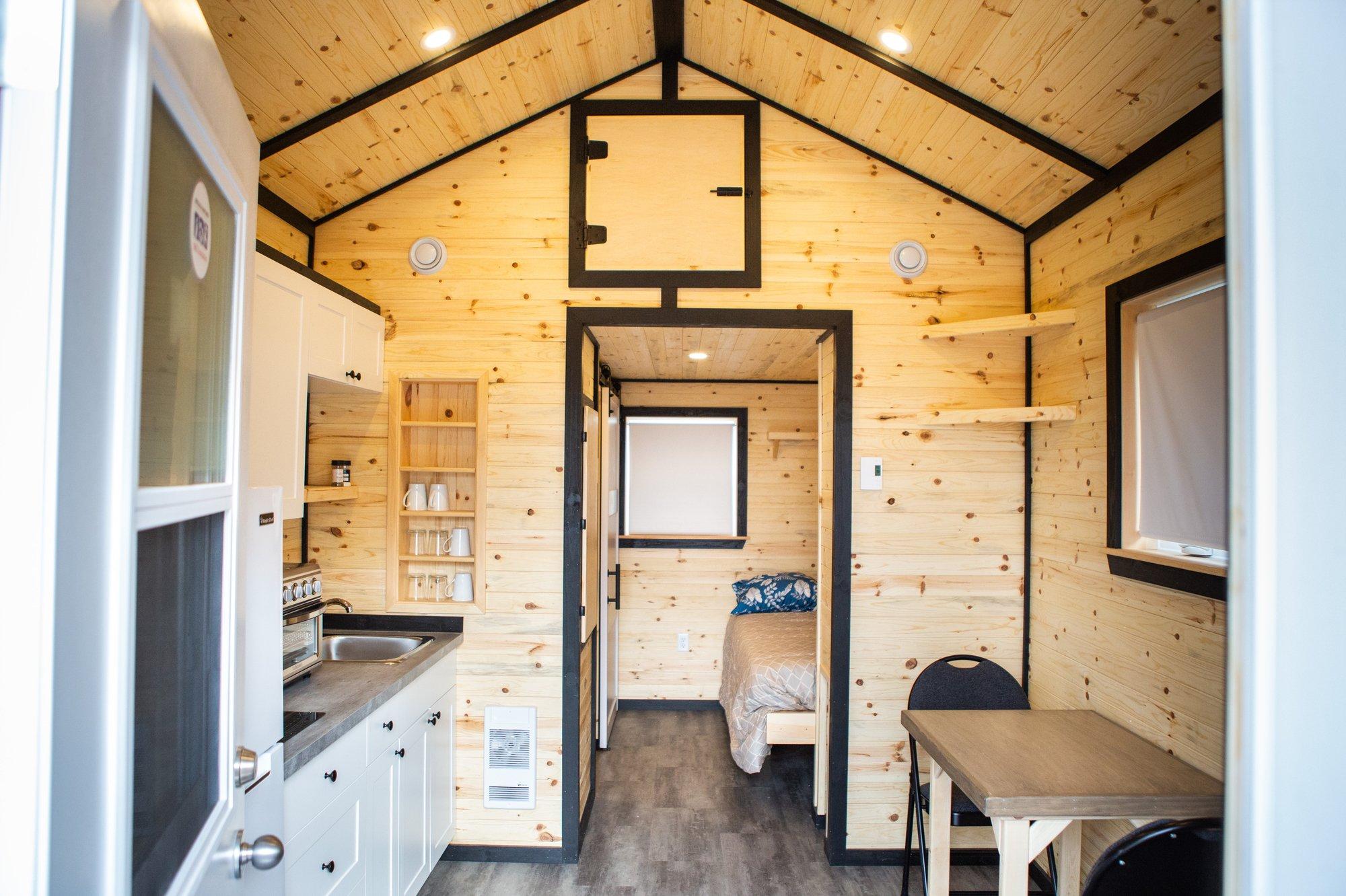 A photo of the interior of a tiny home, complete with a small kitchen and a bed in the background.