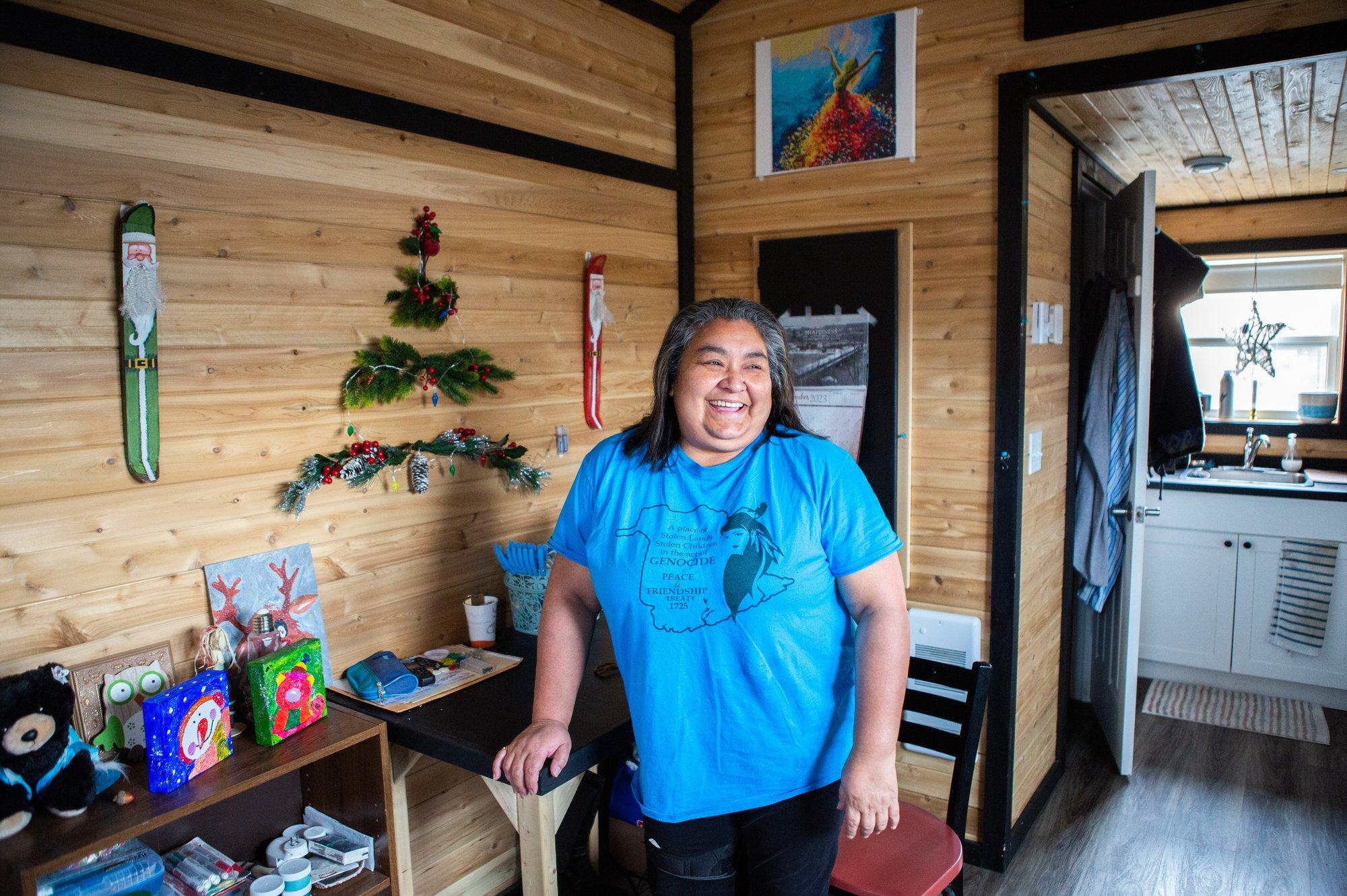 A woman in a blue t-shirt standing in a tiny home with wood walls