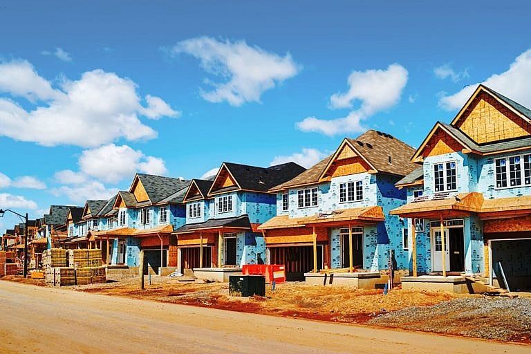 A photo of a row of houses under construction. The sky above them is blue.